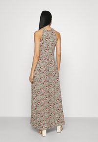 Robe longue fleurie en tissu vert avec des fleurs rouges et roses. Caractérisée par une coupe sans manches et une taille cintrée, s'étendant jusqu'aux chevilles.