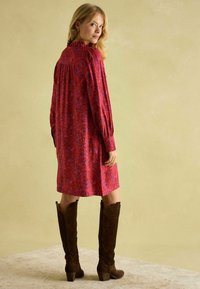 Long-sleeve, knee-length dress in red with floral patterns. Features a ruffled collar and loose fit; paired with brown suede knee-high boots.
