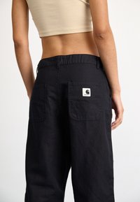 Pantalones de pierna ancha negros, hechos de una tela duradera, que cuentan con dos bolsillos traseros y un logo en forma de parche. La cinturilla es elástica para mayor comodidad.