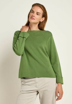 Grüner Pullover mit lässigem Schnitt, geripptem Stoff und langen Ärmeln. Mit einem runden Halsausschnitt und gesplitteten Bündchen gestaltet. Stylisch kombiniert mit hellbeigen Hosen.