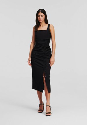 Sort midi-kjole med firkantet udskæring, ruchede sider og en slids i siden. Lavet af glat stof; har et elegant, tætsiddende design.