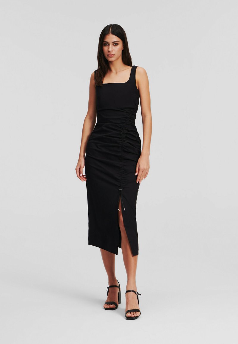 Robe noire midi avec un décolleté carré, des côtés froncés et une fente sur le côté. Fabriquée en tissu lisse, elle présente un design élégant et ajusté.