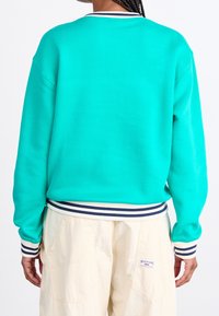 Suéter en turquesa brillante con puños y dobladillo de rayas en navy y blanco acanalados. Material suave, corte relajado y escote de crew.