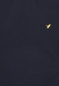 Tissu bleu foncé texturé avec un petit colibri jaune brodé près du côté supérieur droit.