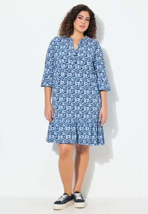 Blau gemustertes Kleid mit Kragen, 3/4-Ärmeln und einem ausgestellten Rüschensaum. Kombiniert mit marineblauen Sneakers für einen lässigen Look.
