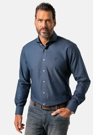 Camicia dress blu navy con maniche lunghe, chiusura con bottoni frontale, texture sottile e un piccolo logo sul petto sinistro. Abbinata a jeans in denim chiaro.