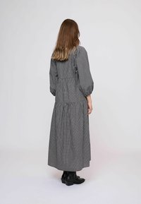 Hosszú, fekete-fehér kockás ruha fodros ujjakkal, összegyűrt derékkal és többrétegű szoknyával. Bokáig érő fekete csizmával viselve.