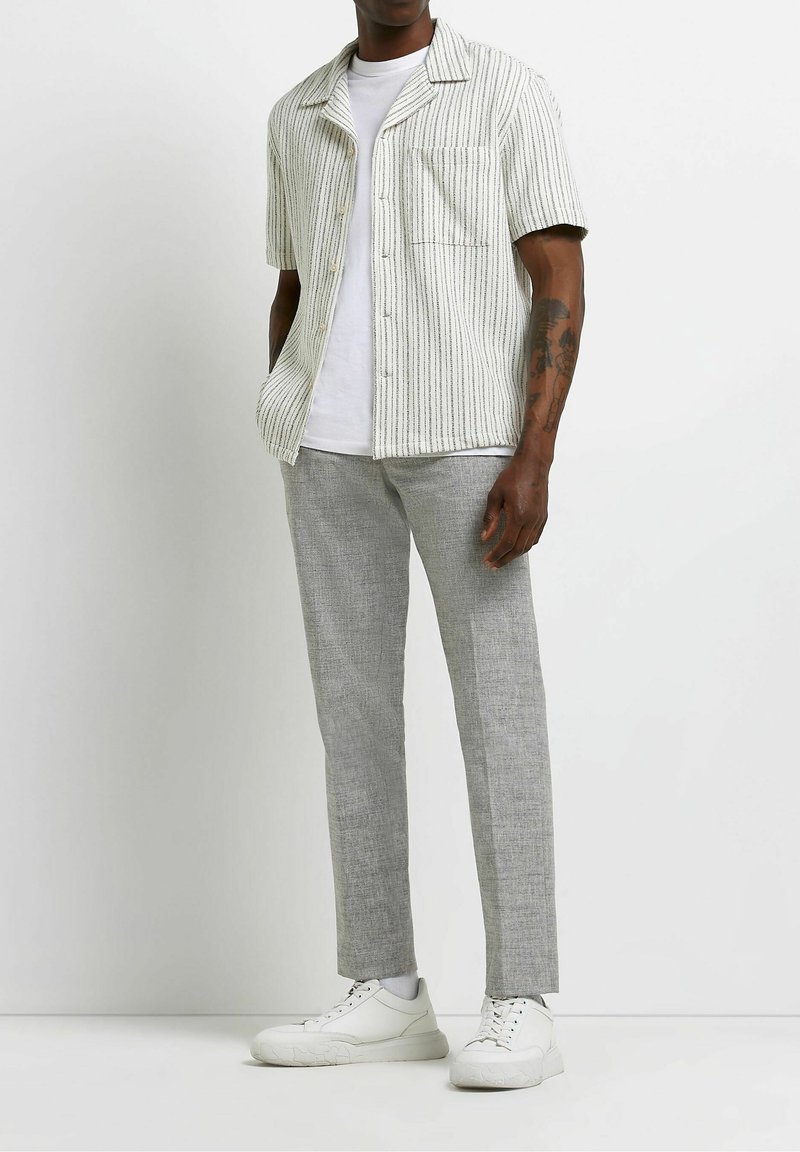 Lyhythihainen vaaleanharmaa ja valkoinen pystykirjallinen nappikauluspaita, yhdistetty vaaleanharmaisiin housuihin ja valkoisiin tennareihin.