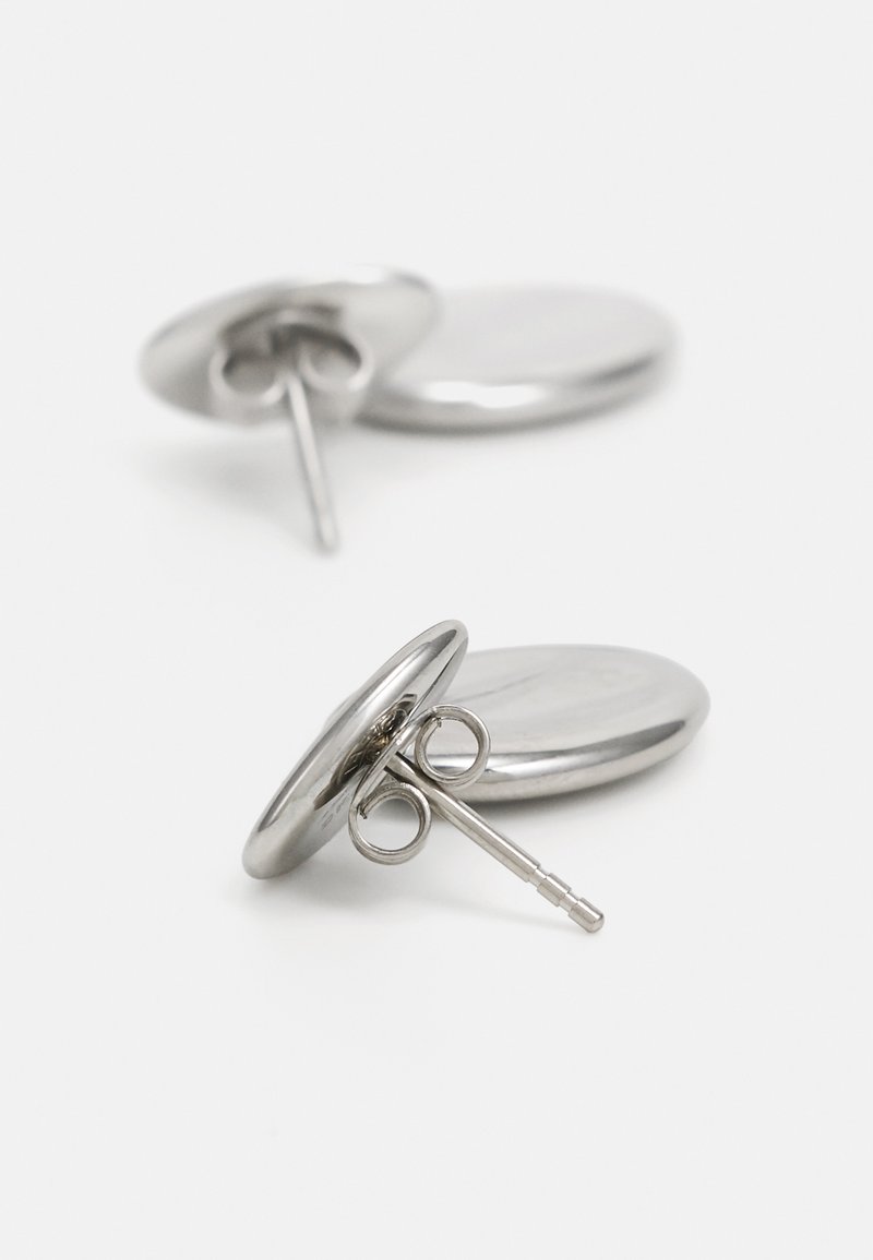 Pendientes de metal con un diseño circular y suave. Acabado plateado pulido, asegurados con un cierre de poste y detalles de hardware redondos.