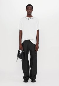 Bílý oversized tričko s potiskem "Just Cavalli" na výstřihu, spárované s černými cargo kalhotami a malou černou kabelkou. Černé boty.