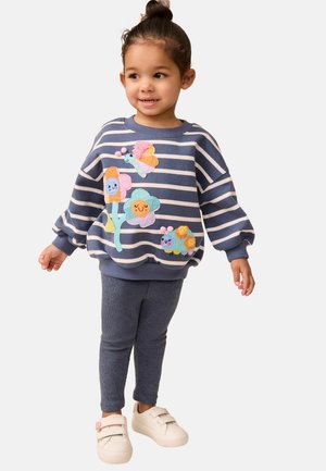 Sudadera a rayas azul con coloridos bordados de flores y mariposas, combinada con leggings navy y zapatillas blancas con acentos en tonos pastel.