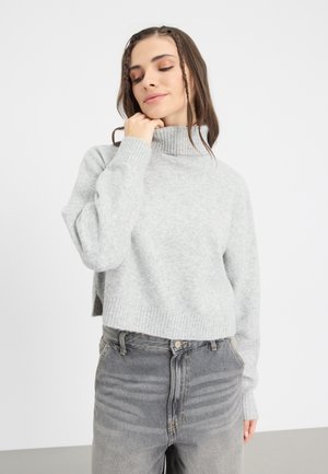 Light gray, cropped turtleneck sweater in a soft knit material, featuring ribbed cuffs and hem. Worn with high-waisted, faded gray jeans.