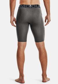 Mann steht barfuß, trägt dunkelgraue, enganliegende Under Armour Kompressionsshorts mit gebrandeter Taille, von hinten vor weißem Hintergrund abgebildet.
