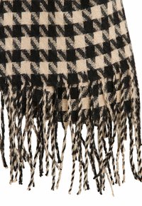 Bufanda de cuadros en negro y beige con textura tejido, que presenta bordes con flecos. El diseño incluye bloques alternos sólidos y con patrón.