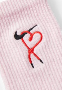 Šviesiai rožinės juostuotos kojinės su juodu ir raudonu išsiuvinėtu dizainu, primenančiu širdį ir Nike logotipą. Minkšta tekstūra, elastingas atidarymas.