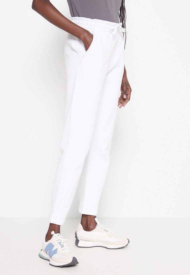 Weiße Joggerhosen mit Seitentaschen, elastischem Kordelzug, schmaler Passform, kombiniert mit beigen Turnschuhen mit blauen und grauen Akzenten.