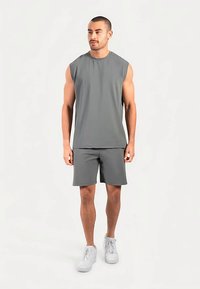 Débardeur et short de sport gris en tissu léger, assortis à des baskets blanches, présentés sur un mannequin masculin debout.