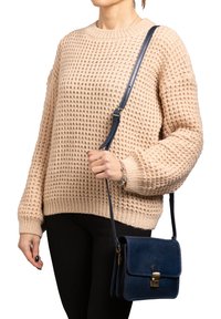 Maglione beige lavorato a maglia con una vestibilità comoda, abbinato a una piccola borsa a tracolla in pelle blu navy con pattina frontale e chiusura dorata.