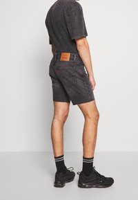 Black denim shorts with a frayed hem and five pockets. Worn with a black tee and black sneakers featuring white-striped socks.