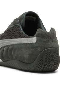 Zapatilla deportiva de ante gris con paneles de malla, suela de goma y parte trasera texturizada. Presenta una franja plateada y el logo de Puma en el talón.