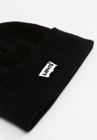 Berretto a maglia nero con risvolto, presenta un'etichetta bianca con il logo Levi's cucita su un lato. Il tessuto ha una finitura liscia e strutturata.
