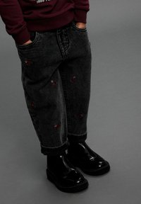 Zwarte spijkerbroek met bloemenborduursel, voorzien van een relaxte pasvorm en opgerolde zoom, gecombineerd met glanzende zwarte enkellaarsjes.