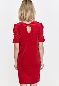 Rotes Samtkleid mit kurzen Puffärmeln, einem Schlüssel-Ausschnitt im Rücken und einer taillierten Silhouette. Geschmeidige Textur und knielanger Saum.