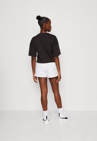 T-shirt nera cropped abbinata a pantaloni corti bianchi. L'outfit presenta una vestibilità rilassata, maniche corte e un design semplice. Footwear è bianco.