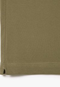 Tessuto verde oliva con una superficie texturizzata, dotato di orlo dritto e spacchi laterali per facilitare il movimento. Cuciture resistenti visibili.