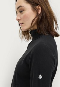 Zwarte fleece fleecetrekker met een hoge kraag, voorzien van een gestructureerd oppervlak en een klein geborduurd embleem op de linkermouw.