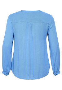 Blusa de manga larga azul claro con escote redondo, detalle plisado en la parte trasera y puños abotonados. Está fabricada con una suave tela texturizada.