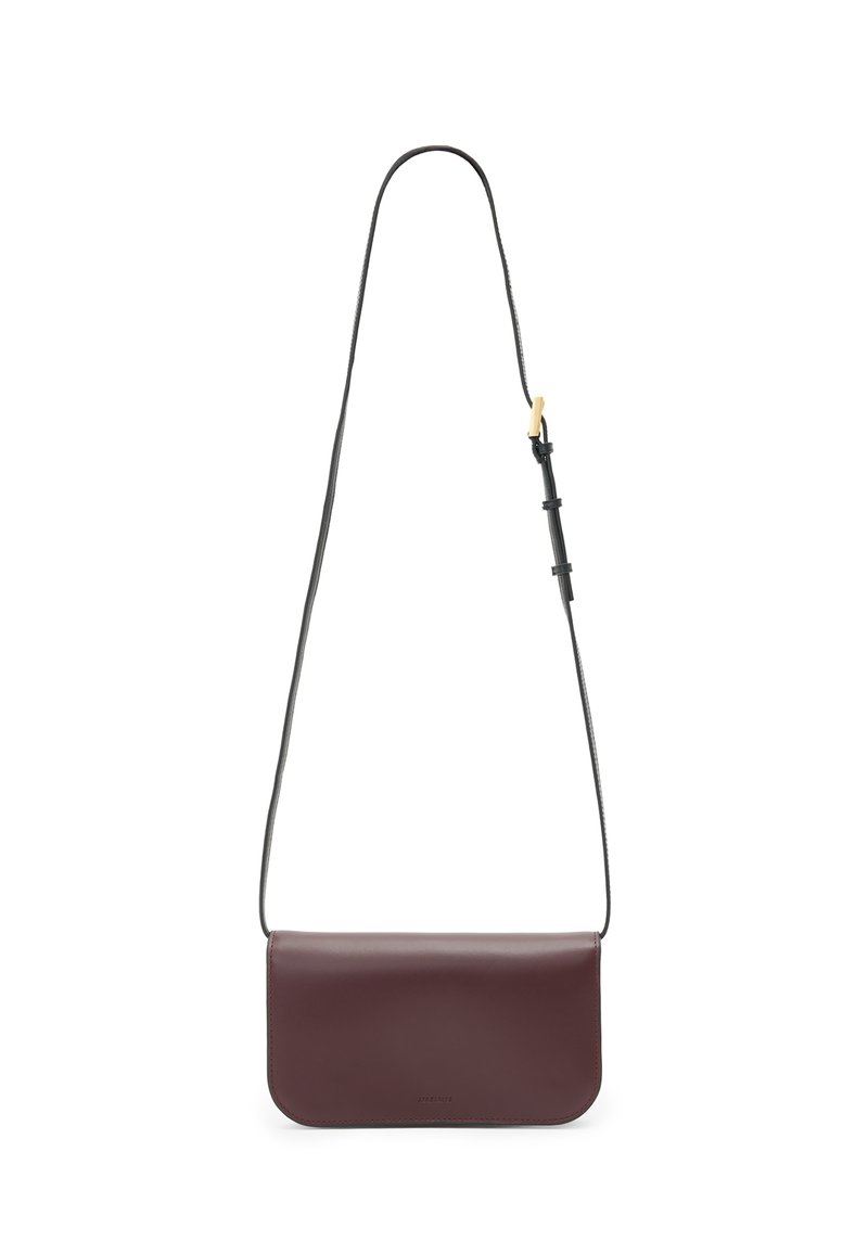 Burgundy läderaxelväska med en ren design, platt form och en tunn svart justerbar rem. Subtil märkning på framsidan.