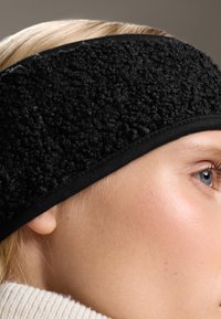 Svart fleece-huvudband med texturerad yta och släta svarta kanter. Närbild som framhäver tygets mjukhet och form.