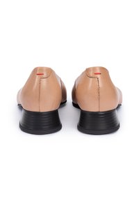 Beige Leder Schuhe mit glatter Oberfläche, runder Form und schwarzen Gummifersen. Sie verfügen über dezente rote Akzente in der Nähe der hinteren Naht.