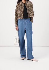 Cropped jas met luipaardprint, zwart topje, losse blauwe spijkerbroek, een witte handtas vasthoudend, lichtgekleurde platte schoenen dragend.