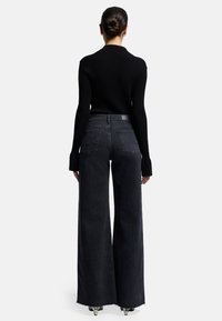 Maglione nero a coste abbinato a jeans a gamba larga a vita alta, con orlo sfilacciato e due tasche posteriori.