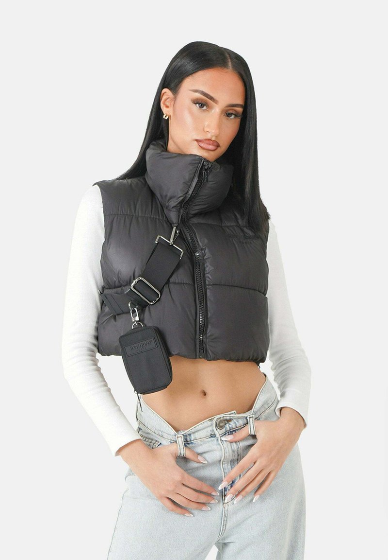 Schwarze Steppweste mit hohem Kragen, Reißverschluss und Seitentasche. Trägt man über einem weißen Langarmshirt, kombiniert mit hochtaillierten Jeans.