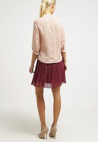 Jasnoróżowa, jedwabista bluzka z rękawami o długości trzech ćwierci. Połączona z bordową, plisowaną spódnicą, która sięga powyżej kolana. Beżowe szpilki.