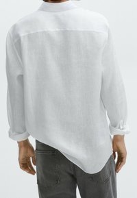 Witte linnen shirt met een zichtbare geperste stof, met knoopsluiting bij de kraag en opgerolde mouwen, gecombineerd met donkergrijze broeken.