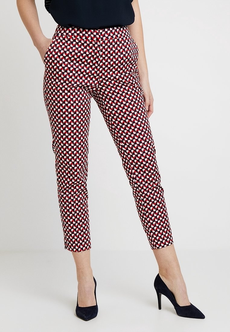 Pantalon slim à motifs rouges et blancs, taille haute avec poches latérales, associé à des chaussures à talons noires.