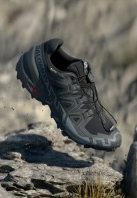 Schwarzer Trailrunning-Schuh mit einem strukturierten Mesh-Obermaterial, reflektierenden Akzenten und einer gepolsterten Sohle. Verfügt über ein sicheres Schnürsystem und ein Logo.