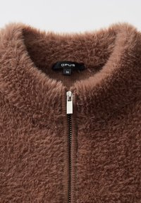 Bruine fuzzy zip-up jasje met hoge kraag en zilveren rits, maat 36, merkembleem "OPUS" zichtbaar binnen de kraag.