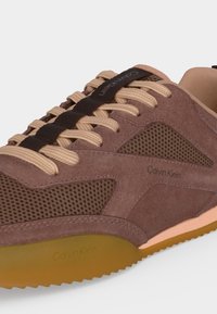 Καφέ σουέτ και δίχτυ το sneaker Calvin Klein με μπεζ κορδόνια, μαύρη ριγωτή λωρίδα με λογότυπο και υφασμένο καουτσούκ σόλα.