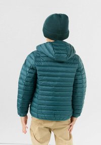 Turkooizen pufferjack met capuchon, voorzien van horizontale doorgestikte secties. Gecombineerd met een bijpassende gebreide muts. Zichtbaar stiksel detail.