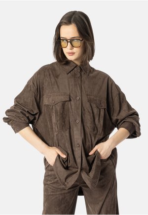 Brun roughe skorte med knappesteng foran, to brystlommer og rullede ermer, kombinert med matchende bukser. Glatt tekstur og avslappet passform.