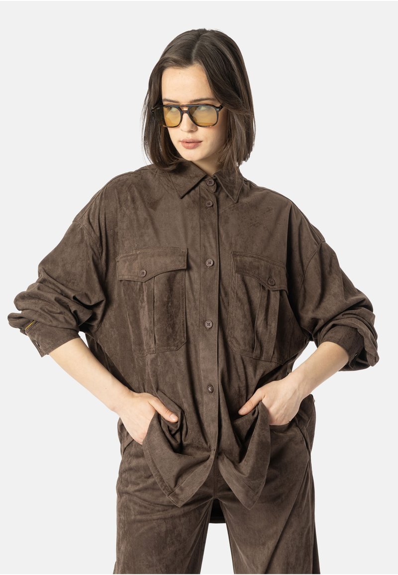 Brun roughe skorte med knappesteng foran, to brystlommer og rullede ermer, kombinert med matchende bukser. Glatt tekstur og avslappet passform.