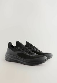 Baskets de sport noires avec une tige en mesh respirant, des détails texturés, et une semelle rembourrée avec un motif en vagues sur les côtés.