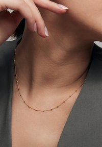 Złoty naszyjnik łańcuszkowy z małymi, równomiernie rozmieszczonymi sferycznymi akcentami. Minimalistyczny design z delikatną teksturą, eksponowany na szarym tle.