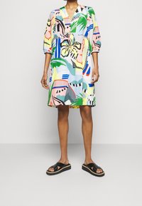 Abito multicolore con scollo a V, maniche a sbuffo e motivi tropicali. Indossato con sandali neri con fasce incrociate e suola testurizzata.