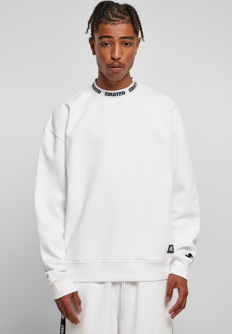 Hvid sweatshirt med et sort "STARTER" logo på kraven. Den har en løs pasform, ribbede manchetter og et lille mærke på kanten.